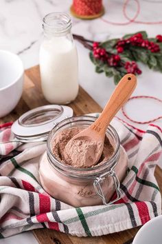 a wooden spoon is in a jar filled with cocoa powder on a plaid towel next to two jars of milk