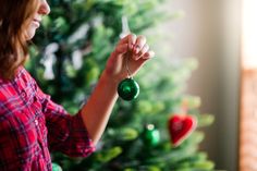 a woman holding a green ornament in front of a christmas tree with ornaments