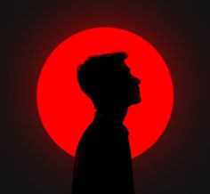 the silhouette of a man in front of a bright red sun with his head turned to the side