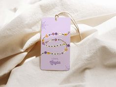 a purple tag with the words thank you and beads on it sitting on a white sheet