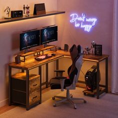 a computer desk with two monitors and a keyboard on it in front of a neon sign that says don't worry the laptop