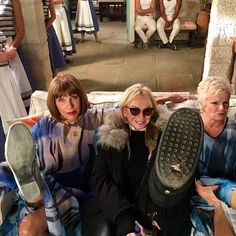 three women sitting on a couch with one holding a shoe and the other wearing sunglasses