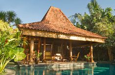 a small wooden house with a pool in the foreground and palm trees around it