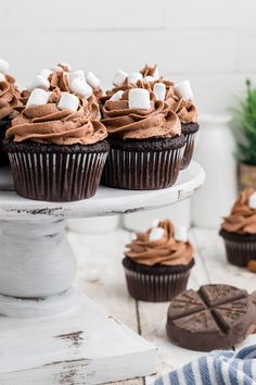 chocolate cupcakes topped with marshmallows on a white cake platter