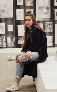 a woman sitting on top of a white bench next to a wall covered in posters