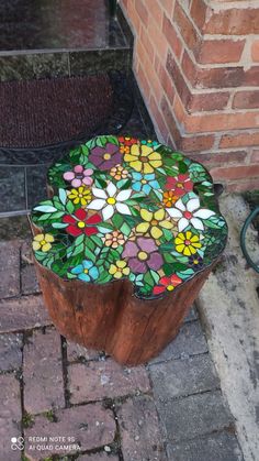 a wooden stump with stained glass flowers on the top and bottom, sitting in front of a brick wall