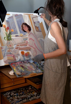 a woman in an apron is painting on the easel and she is looking at it