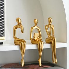 three gold sculptures sitting on top of a white shelf next to a black and white book