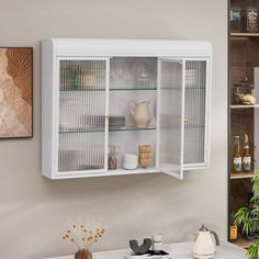 a white cabinet with glass doors is in the corner of a room next to a plant