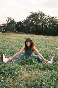 a woman sitting in the middle of a field with her legs spread out and smiling