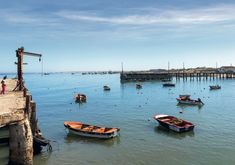 several small boats floating on top of a body of water next to a wooden pier