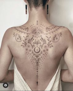 the back of a woman's neck with an intricate tattoo design on her left shoulder