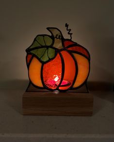 a stained glass pumpkin sitting on top of a wooden stand with a lit candle in it