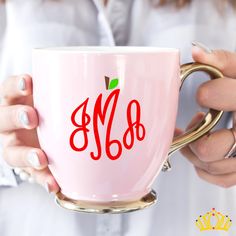 a woman holding a pink coffee cup with an apple on the front and red lettering