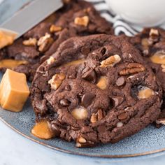 chocolate cookies with pecans and caramel chunks on a plate next to a glass of milk