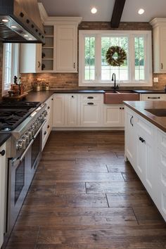 a large kitchen with white cabinets and wood flooring on the counter tops, along with a wreath hanging above the stove