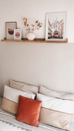 a bed with two pictures on the wall above it and an orange pillow sitting on top of it