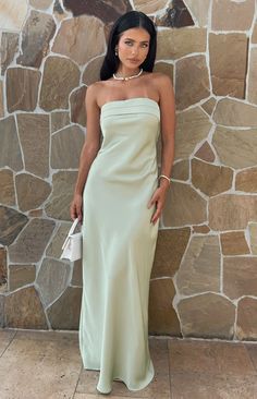 a woman standing in front of a stone wall wearing a strapless dress and holding a white purse