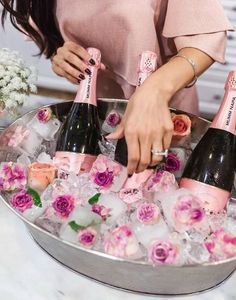 a woman holding three bottles of champagne in an ice bucket filled with flowers and ice