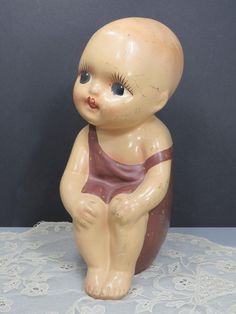 a ceramic baby doll sitting on top of a white lace tablecloth with a black background