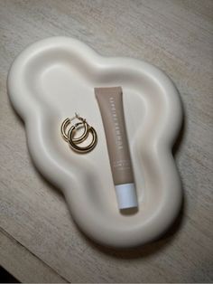 a tube of lip gloss sitting on top of a white plate next to a gold ring