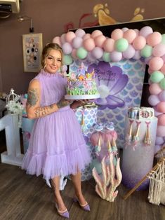 a woman in a purple dress holding a cake and standing next to a mermaid themed backdrop