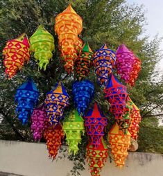 many colorful kites hanging from a tree in front of a wall and some trees