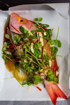 a white plate topped with fish and veggies on top of parchmented paper