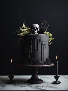 a black cake with white frosting and skulls on top, surrounded by candles in front of it