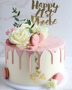 a birthday cake decorated with pink and white icing, flowers and gold leaf decorations