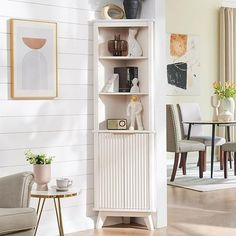 a white bookcase in the corner of a living room with chairs and table next to it