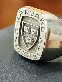 GENUINE HARVARD UNIVERSITY 18K WHITE GOLD SIGNET SCHOOL RING SIZE 9.5 - 10. ITS APPRXIMATELY 11.9 GRAM OF SOLID 18K GOLD. (No stone weight) This is my personal graduate school signet ring from Harvard University, Faculty of Arts and Science. It's Josten brand, 18k solid white gold, and a "hand engraved" signet ring. It is not laser engraved like today's typical ring. In fact, this handmade design was discontinued, and now Josten makes easy laser-engraved signet rings. My name is lightly engraved Arts And Science, School Rings, College Education, Signet Rings, Harvard University, Ring Pictures, Graduate School, Book Store, Handmade Design