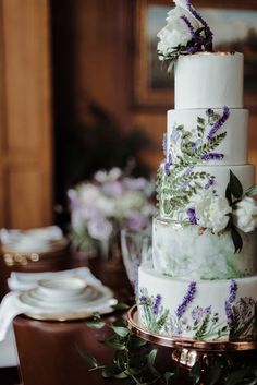 a three tiered cake with purple and white flowers on it sitting on top of a table