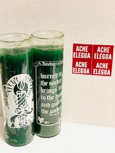 two green candles sitting next to each other on a white surface with red stickers