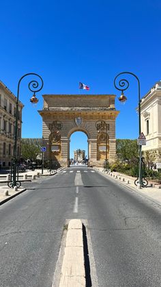 an empty street in the middle of a city with buildings on both sides and a large arch at the end