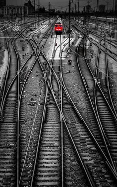 a red train traveling down tracks next to another set of railroad tracks in black and white