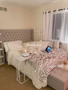 a bed with a laptop on top of it in front of a window and curtains