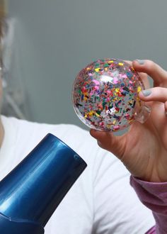 a woman holding up a glass ball with sprinkles on it