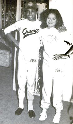 a man and woman in baseball uniforms standing next to each other with their arms around each other