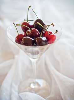 a martini glass filled with cherries on top of a white cloth covered tablecloth