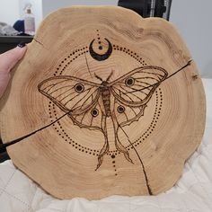 a wooden plate with a moth on it and a crescent moon in the middle, sitting on a bed