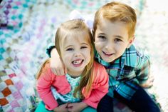 two young children sitting next to each other on a quilted bed spread with their arms around each other