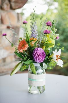 a vase filled with lots of flowers on top of a white table covered in greenery