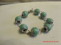 a green and silver bracelet with glass beads on a white tablecloth covered surface,