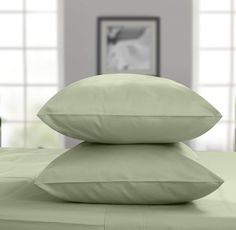 three pillows stacked on top of each other in front of a bed with green sheets