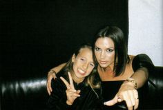 two beautiful young women sitting next to each other in front of a black couch and pointing at the camera