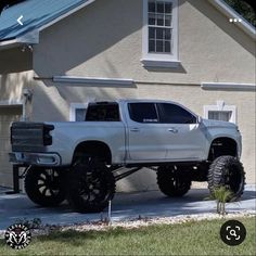 a white truck is parked in front of a house with large tires on the rims