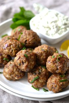 some meatballs are on a plate next to a small bowl of dip and lemon wedges