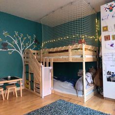 a room with bunk beds and a tree on the wall, in front of a blue wall