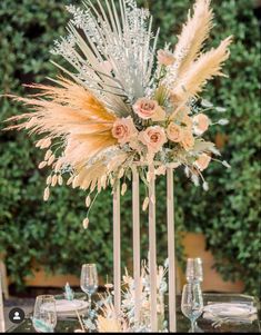 a tall centerpiece with flowers and feathers on top of a glass table set for a wedding reception